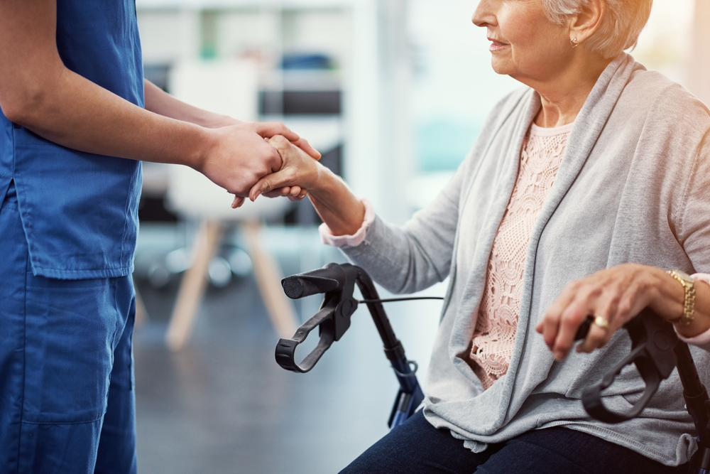 Im here for you…an unrecognizable female nurse holding her senior patients hand in comfort.