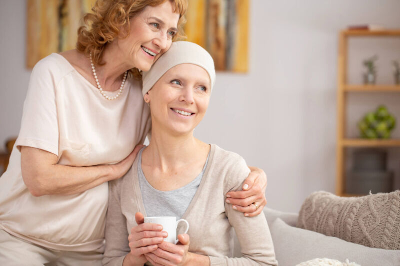 Smiling woman with a headscarf being embraced by a loved one on a couch, illustrating emotional support and comfort during breast cancer hospice care