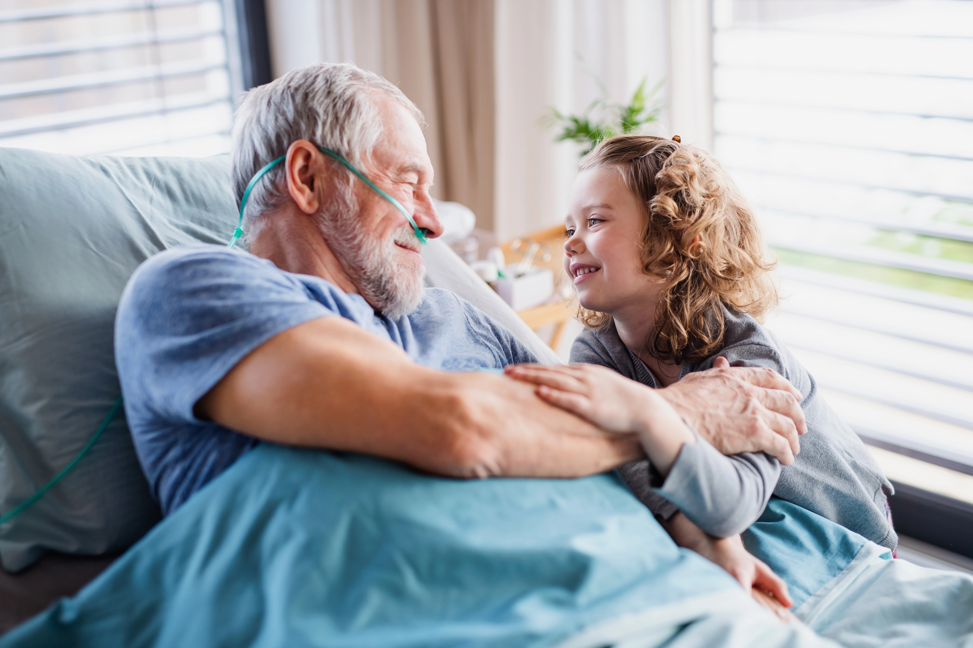 Smiling elderly man in hospice bed with oxygen tube holds and looks at young girl, illustrating liver cancer hospice timeline