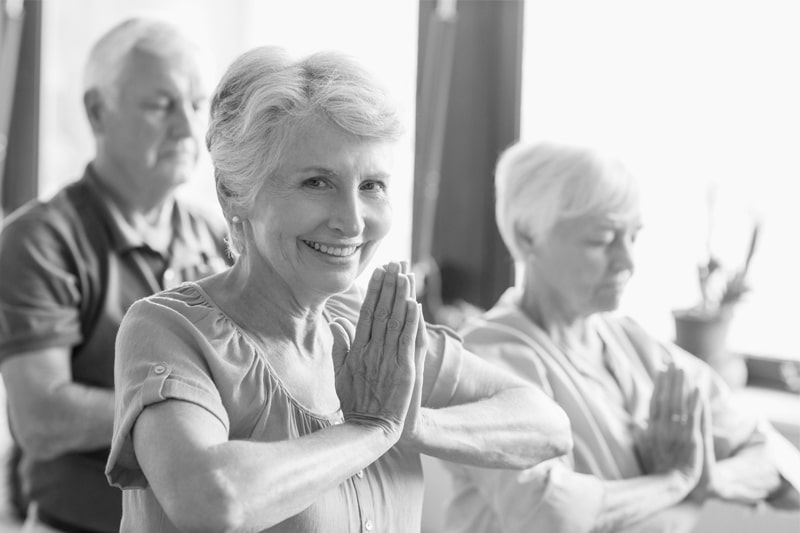 A smiling, happy elderly woman practicing yoga in order to manage her dementia life expectancy